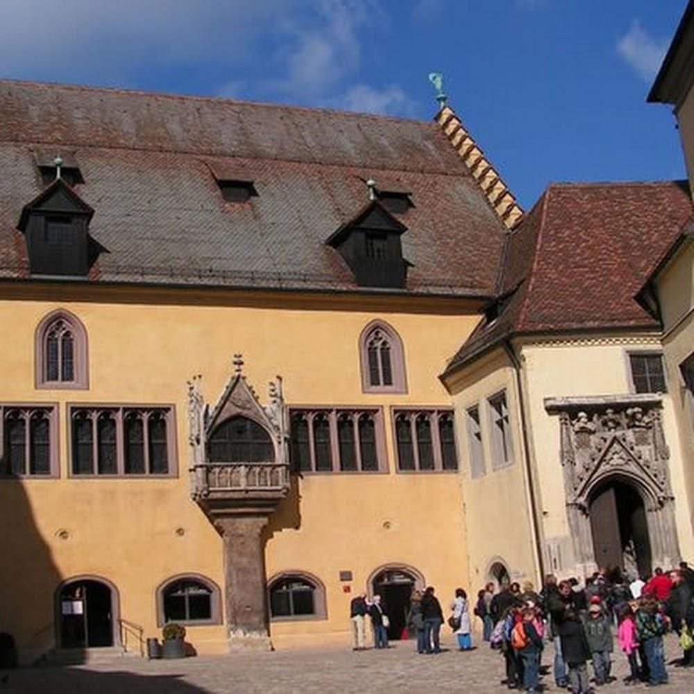 A yellow building with a stone tower and people walking in front. Landmark: Neues Rathaus, Munich.